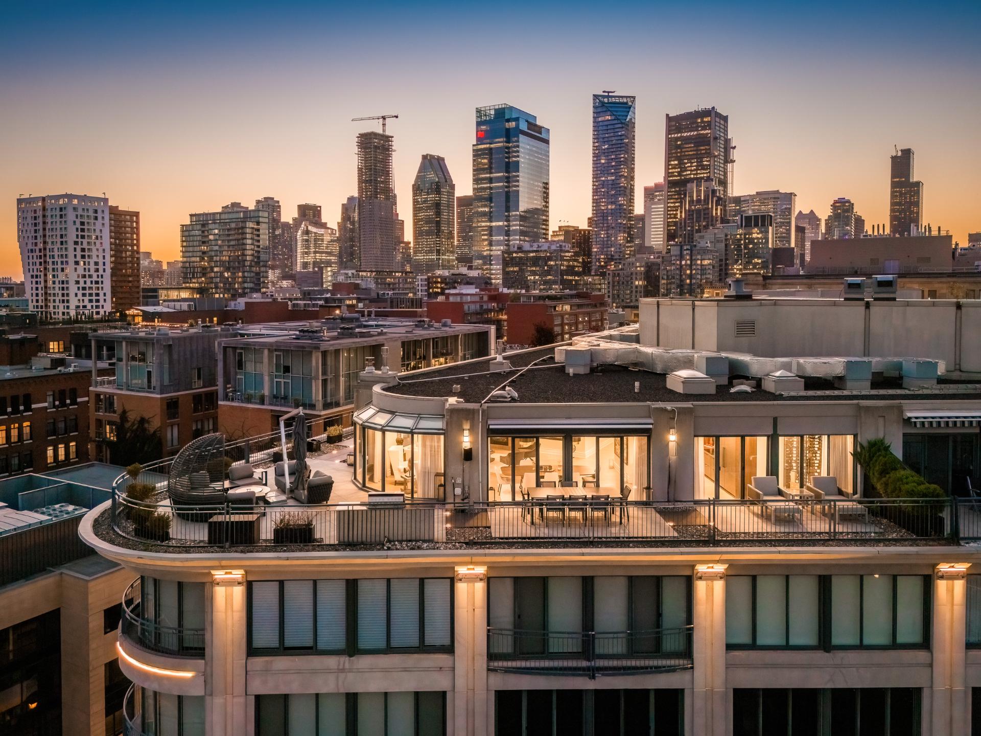Le penthouse du 1 McGill au crépuscule, sa terrasse ceinturante éclairée devant la silhouette du centre-ville de Montréal