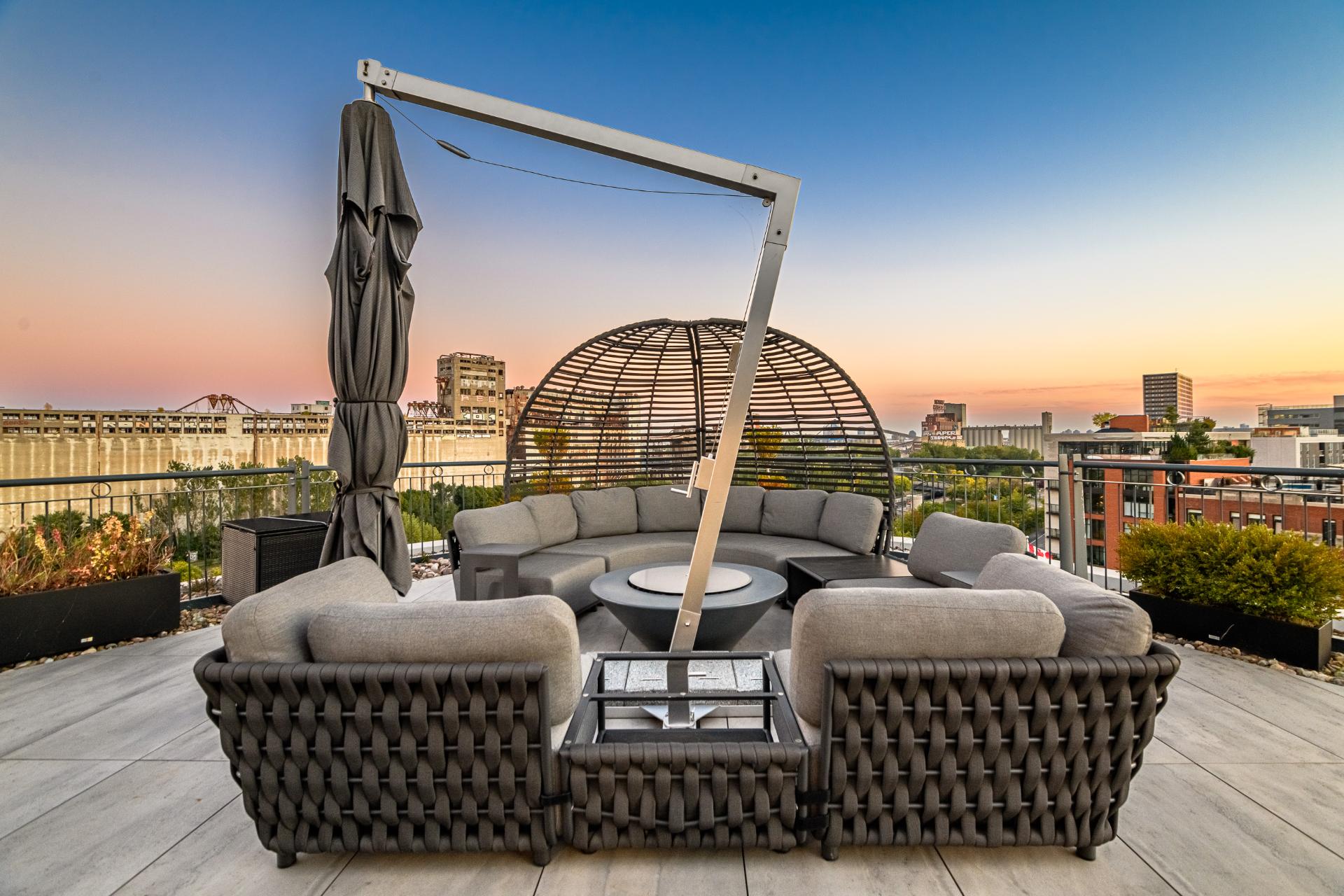 Terrasse privée du penthouse aménagée en salon extérieur, face à la silhouette du centre-ville au coucher du soleil